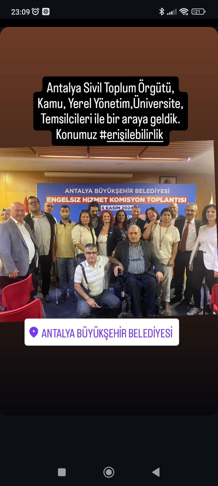 Fotoğrafta, bir grup insan bir araya gelmiş ve bir etkinlikte poz veriyorlar. Arkalarında "Antalya Büyükşehir Belediyesi Engelsiz Hizmet Komisyon Toplantısı" yazılı bir afiş var. Afişte ayrıca "6 Kasım 2023" tarihi belirtilmiş. Üst kısımda ise "Antalya Sivil Toplum Örgütü, Kamu, Yerel Yönetim, Üniversite, Temsilcileri ile bir araya geldik. Konumuz #erişilebilirlik" yazıyor. Fotoğrafın alt kısmında "Antalya Büyükşehir Belediyesi" konum etiketi bulunuyor. İnsanlar gülümseyerek kameraya bakıyorlar ve aralarında tekerlekli sandalyede oturan bir kişi de var.